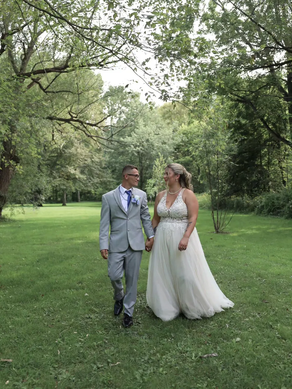 Newlyweds walking hand in hand across a garden lawn