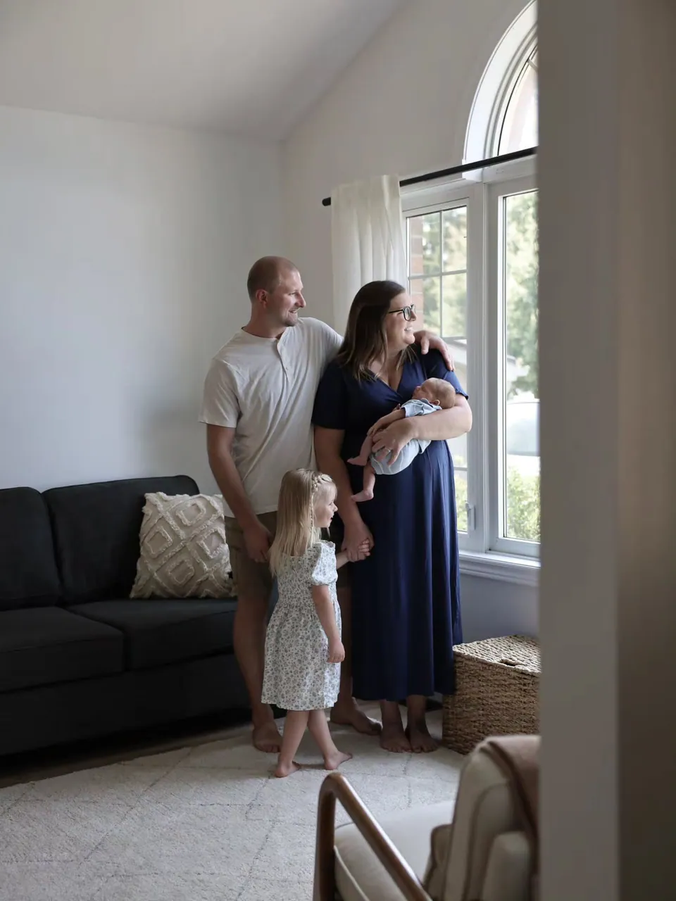 A family at home by a bright window with their newborn